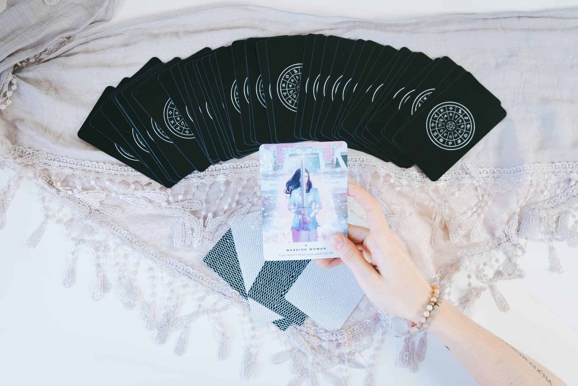 Hand som håller ett tarotkort framför en utspridd kortlek